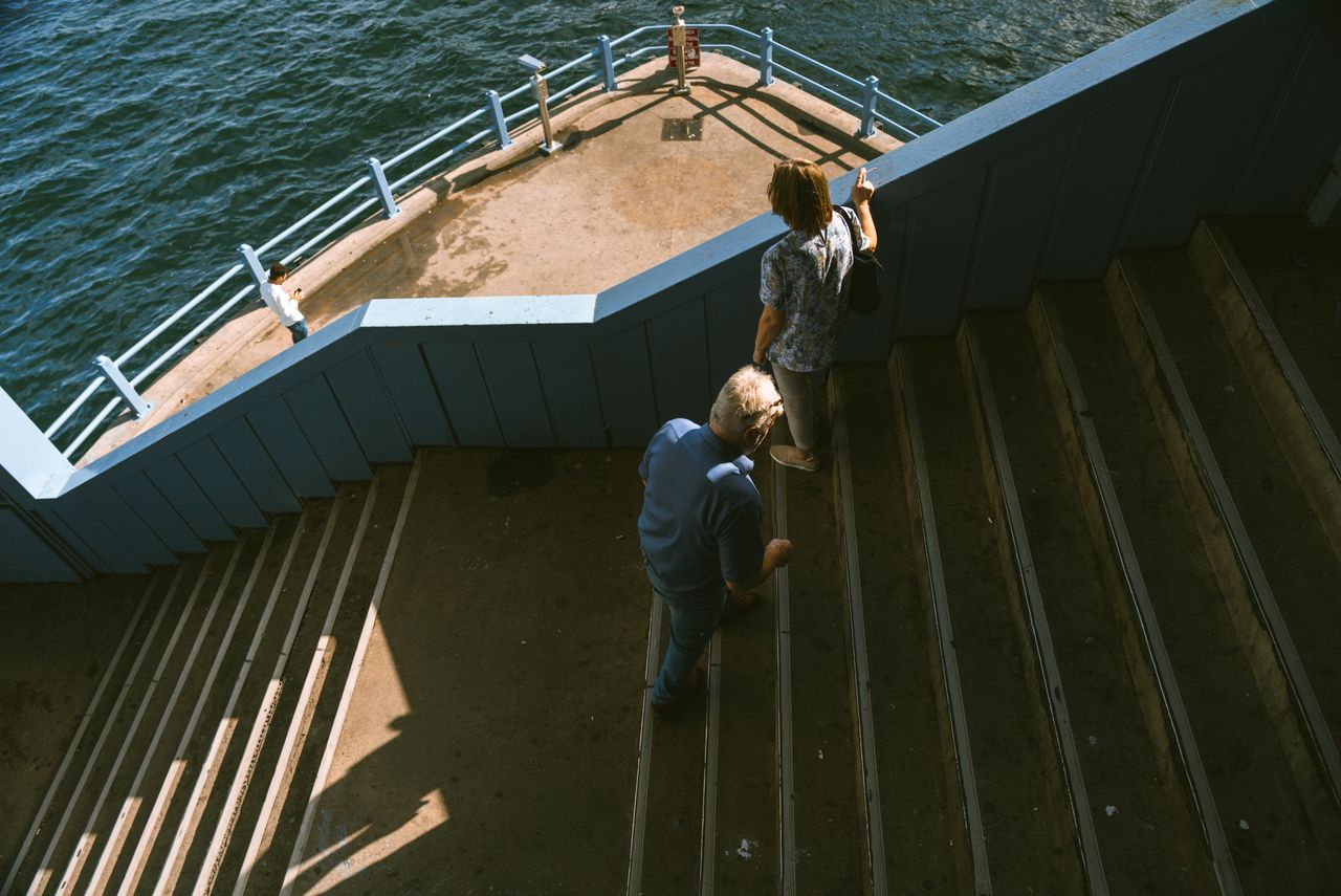 Couple walking down stairs towards a scenic waterfront promenade by the ocean.