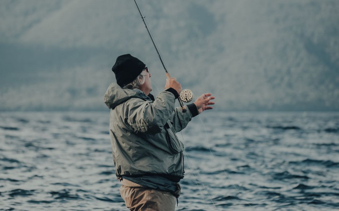 Elderly man enjoys fly fishing at a tranquil lake surrounded by nature.