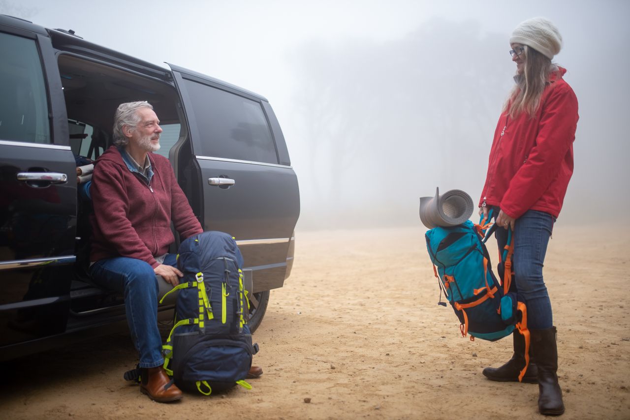 An elderly couple with backpacks preparing for a hike on a foggy day in Portugal.