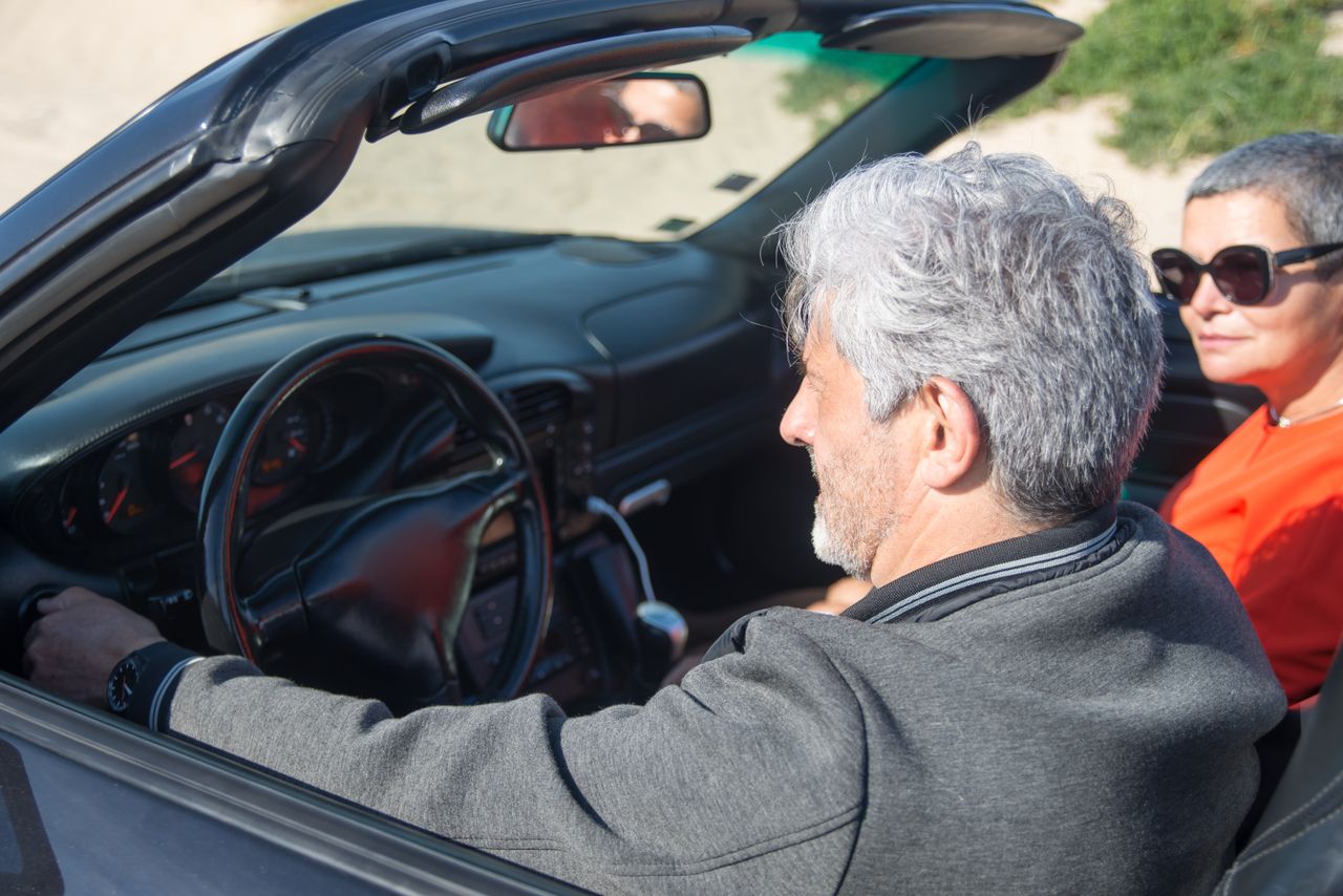 Senior couple enjoying a sunny drive in a convertible through scenic Portugal.