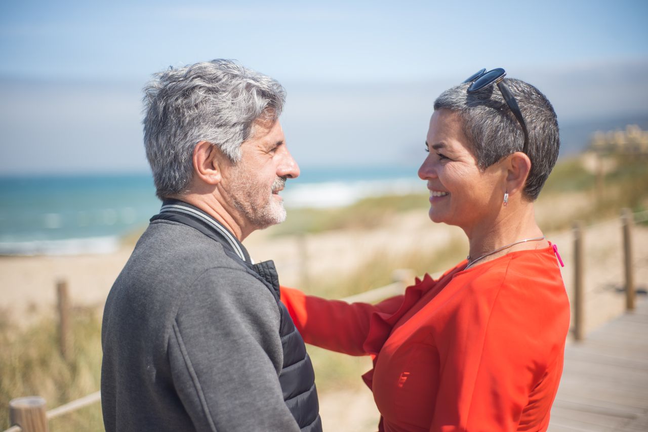 Mature couple smiling lovingly at each other on a sunny beach in Portugal.